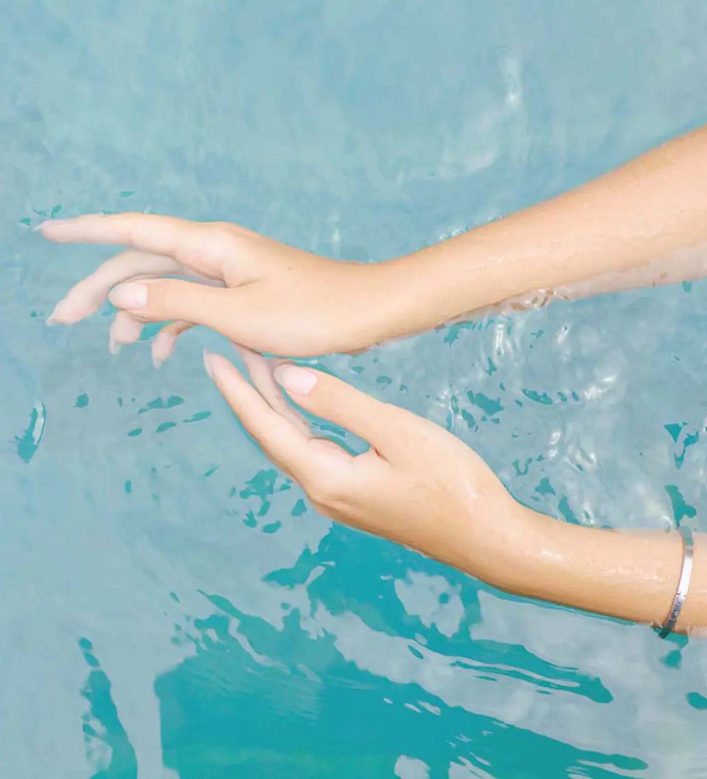 Frauenhände im Wasser, die mit hocheffizientem Sonnenschutz eingecremt sind